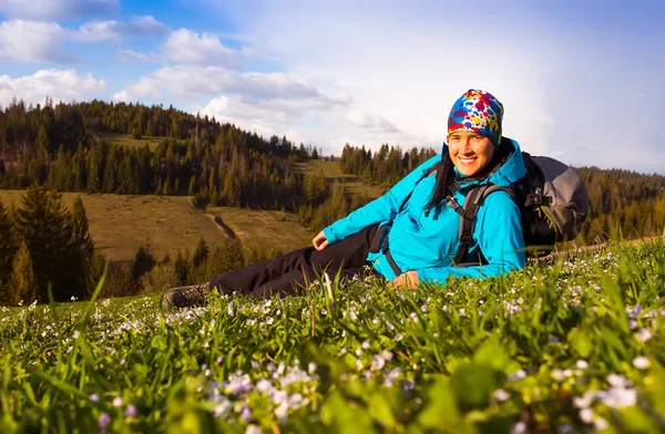 Sano escursionista ragazza in escursione nella natura. Bella giovane donna escursionismo felice siede su un prato. Sullo sfondo bellissime montagne e cielo blu con nuvole — Foto Stock