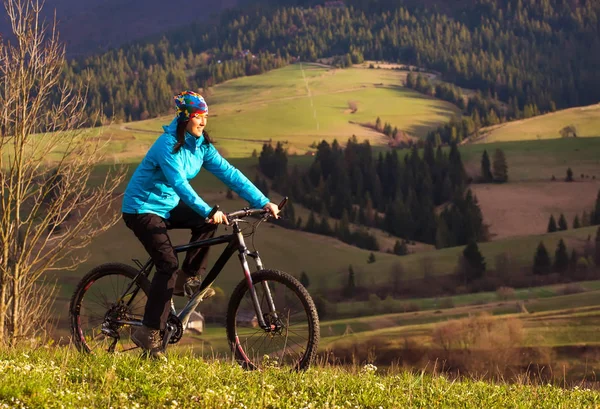 Ciclista de montaña en un día soleado montando en un sinuoso camino de tierra en una zona rural montañosa de bosque verde contra el cielo azul con hermosas nubes — Foto de Stock