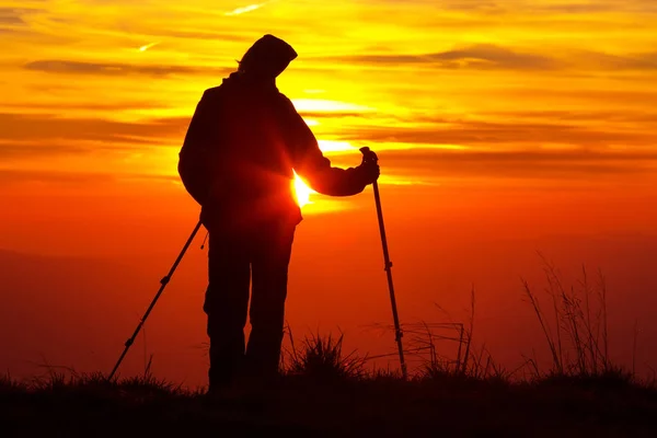 Silhouette di una ragazza sulla cima di una montagna su sfondo arancione fuoco con bastoncini da trekking — Foto Stock