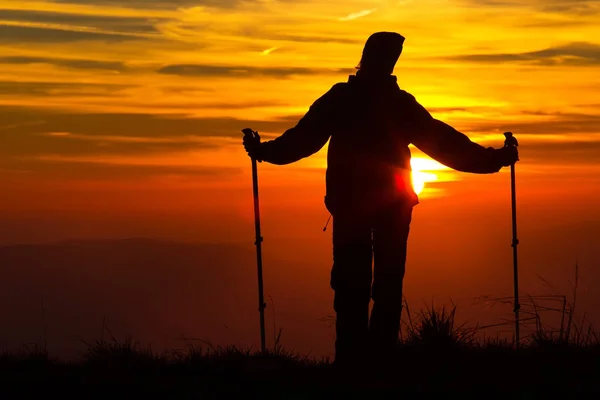 Silhouette d'une fille sur un sommet de montagne sur fond orange vif avec des bâtons de trekking — Photo