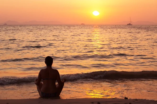 Meditación - Meditar a la mujer del yoga en el atardecer sereno de la playa. Chica relajante en pose de loto en calma zen momento en el agua del océano durante las vacaciones de yoga resort retiro. Chica multirracial . — Foto de Stock