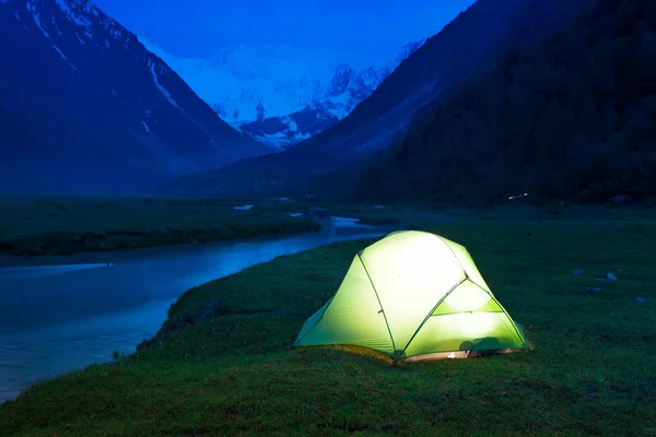 Carpa resplandeciente se encuentra en las orillas de un arroyo de montaña, en medio de altas montañas y picos nevados. Crepúsculo, noche . — Foto de Stock