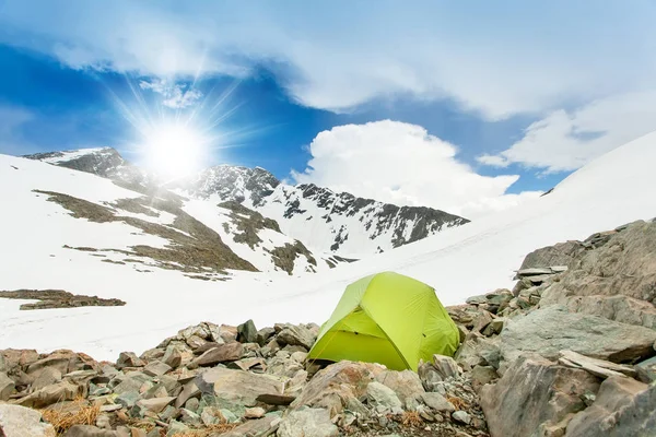 Tent stands in extreme conditions on the rocks. Background blue sky and mountain peaks in the snow. — Stock Photo, Image
