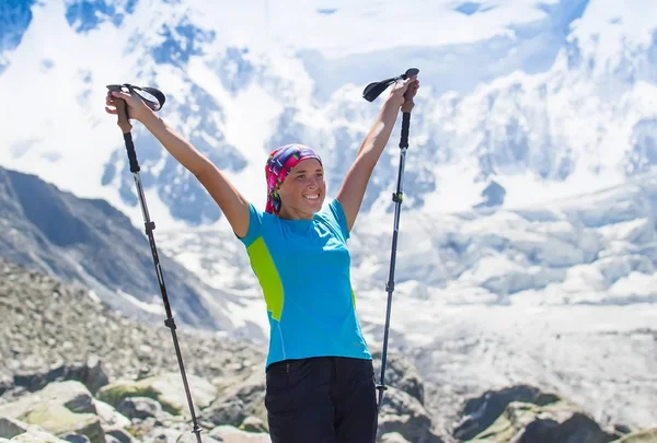 Friska flicka hiker med vandringsstavar att övervinna svårigheter i bergen. Bakgrund av höga berg, glaciärer. — Stockfoto
