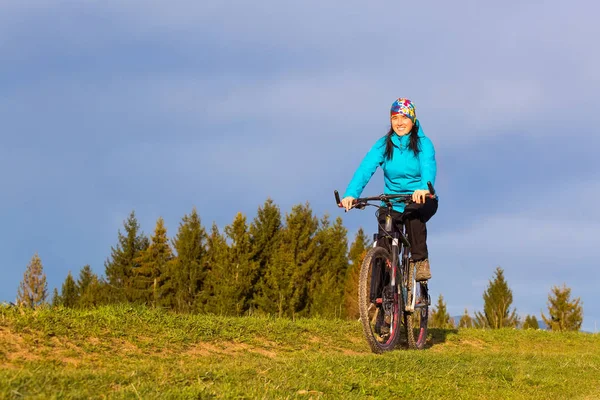 Гірський велосипедист в сонячний день їде на звивистій брудній дорозі в сільській горбистій місцевості зеленого лісу проти блакитного неба з красивими хмарами Ліцензійні Стокові Фото