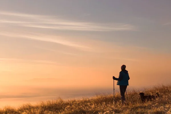 Siluett av en flicka med en ensam sport Trekking pol i dimma på morgonen. Liggande sammansättning, bakgrund berg och soluppgång. — Stockfoto