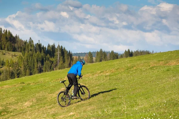 Mountainbiker am sonnigen Tag rollt auf den sanften Hügeln des grünen Waldes gegen den blauen Himmel mit schönen Wolken — Stockfoto