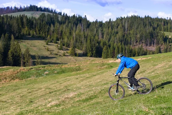 Mountain biker on sunny day rolls on the rolling hills of green forest against the blue sky with beautiful clouds — Stock Photo, Image