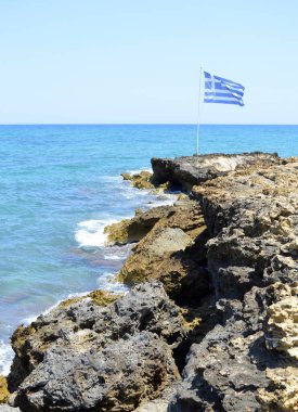 Girit 'teki Kato Gouves kıyıları engebeli sahil kıyısında Yunan ulusal bayrağını dalgalandıran Yunan adalarının en büyük ve en kalabalık adaları.