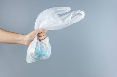 Gri arka planda plastik poşet ve Globe tutan adam.