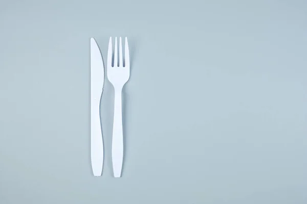 Tenedor de plástico blanco y cuchillo sobre fondo gris con espacio de copia — Foto de Stock