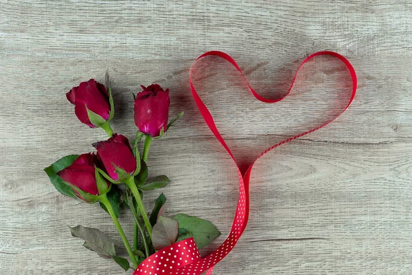 Red rose flower and heart shape ribbon on wood table background.