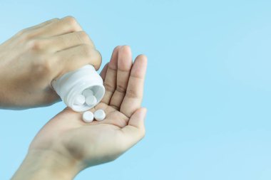 Woman holding white pills on hand against blue background. Medic