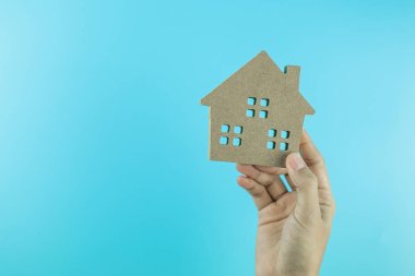 Mavi arka planda el ele tutuşan ev modeli ve metin için kopya alanı. Bankacılık, gayrimenkul, yatırım, finans, tasarruf kavramları