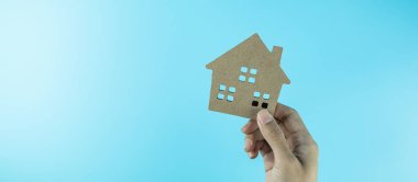 Mavi arka planda el ele tutuşan ev modeli ve metin için kopya alanı. Bankacılık, gayrimenkul, yatırım, finans, tasarruf kavramları