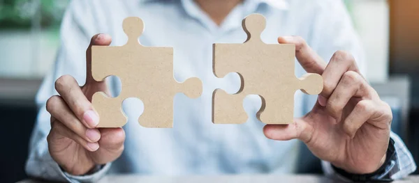 man hands connecting couple puzzle over table, businessman holding wood jigsaw inside office. Business solutions, mission, target, success, goals and strategy concepts