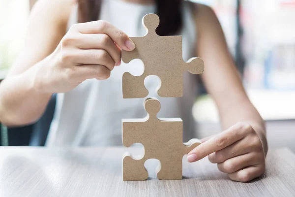 woman hands connecting couple puzzle over table, businesswoman holding wood jigsaw inside office. Business solutions, mission, target, success, goals and strategy concepts