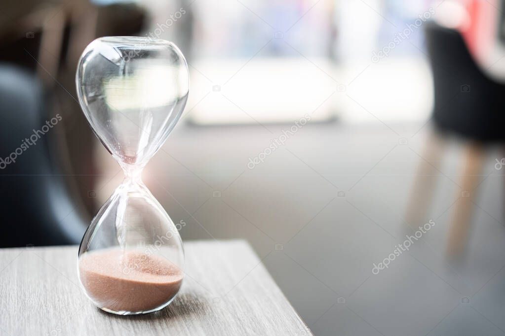 Hourglass on table office with copy space, Sand flowing through the bulb of Sandglass measuring the passing time. countdown, deadline, Life time and Retirement concept