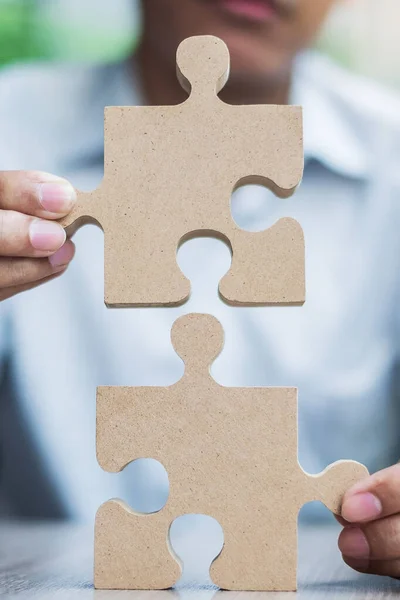 man hands connecting couple puzzle over table, businessman holding wood jigsaw inside office. Business solutions, mission, target, success, goals and strategy concepts