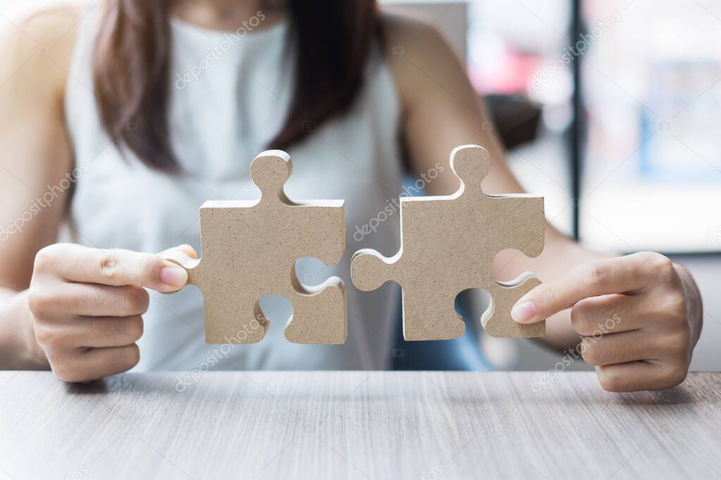 woman hands connecting couple puzzle over table, businesswoman holding wood jigsaw inside office. Business solutions, mission, target, success, goals and strategy concepts