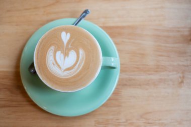 Kafe dükkanındaki ahşap masada bir fincan sıcak sanat kapuçinosu.