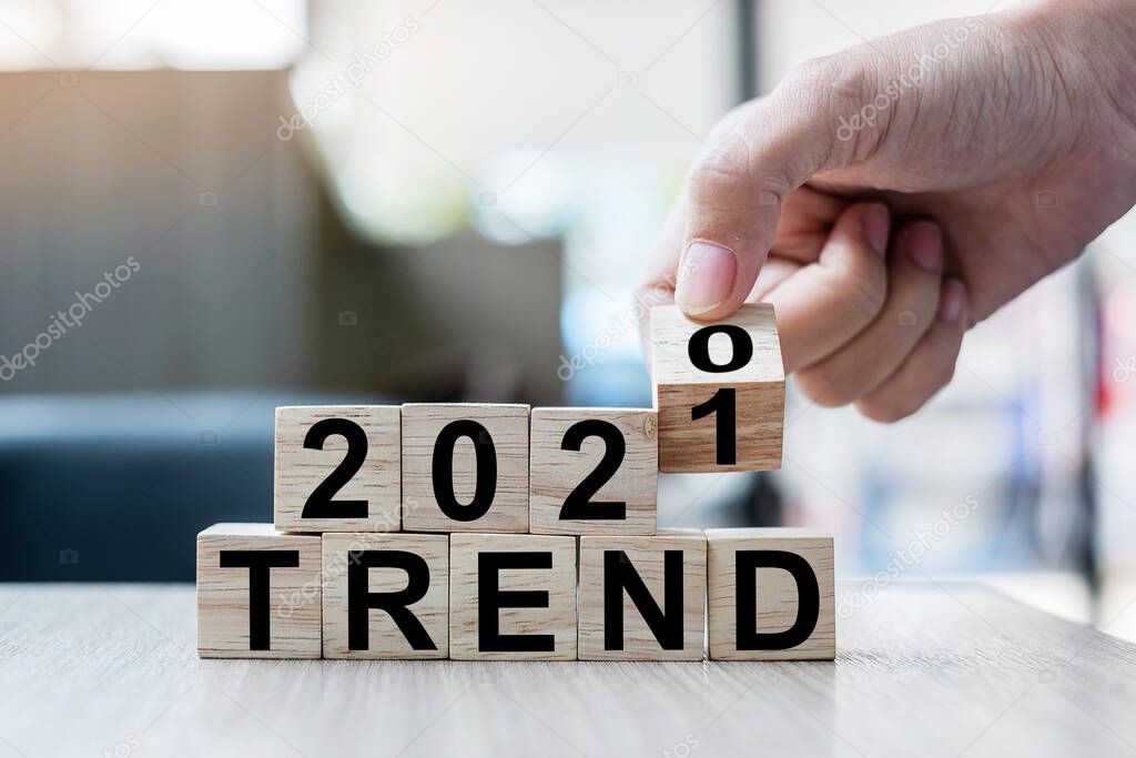 Businessman hand holding wooden cube with flip over block 2020 to 2021 TRENDS word on table background. Resolution, strategy, solution, goal, business and New Year holiday concepts