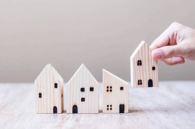 İş kadını masa arkasında ahşap ev modelini tutuyor. Ev, Kriz, Ekonomik Durgunluk, Evsiz, Gayrimenkul, Alış veya Kira ve Emlak kavramı