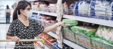 Korumalı maske takan Asyalı kadın süpermarkette ya da markette alışveriş yaparken elinde yiyecek ürünleri bulundurarak koronavirüsü koruyor. Sosyal uzaklık, yeni normal ve covid-19 salgınından sonraki yaşam