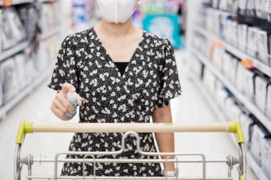 Markette ya da markette alkol spreyi sıkarak alışveriş arabasının yüzeyini temizleyen Asyalı kadın, koronavirüsü korur. Hijyen, yeni normal ve covid-19 salgınından sonraki yaşam