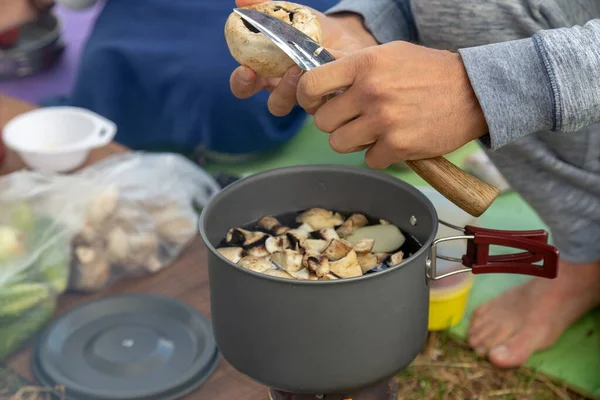 Camping food making. Pasta on pan on tourist fire stove. Camp cooking a mushroom soup at the lake shore.