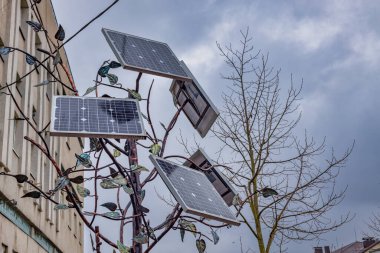Şehir parkında güneş enerjisi ağacı heykeli. Şarj edilebilir gece lambası ve aletler şehirde bedava yer açıyor. Çevresel tema.