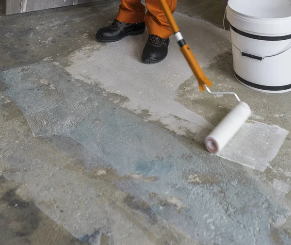 Worker puts primer with roller on concrete floor. Apartment unde — Stock Photo, Image