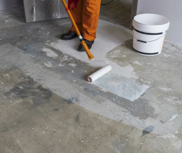 Lavoratore mette primer con rullo sul pavimento di cemento in camera da un — Foto Stock