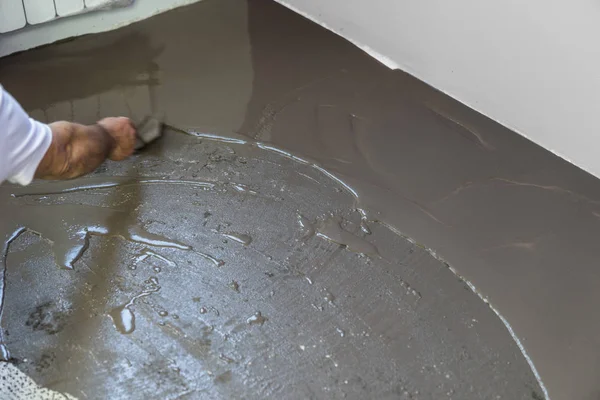 Homem coloca uma mesa de auto-nivelamento com espátula no chão de concreto. H — Fotografia de Stock