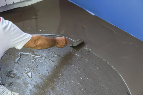 Trabajador pone una regla de nivelación de uno mismo en el piso de cemento en casa Fotos De Stock