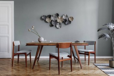 Modern ve şık yemek odaları, göz alıcı ahşap masa, zarif sandalyeler ve tasarım dekorasyonu. Şablon. Ev dekoru. Gri arka plan duvarı. İç tasarımın minimalist kavramı.
