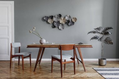 Modern ve şık yemek odaları, göz alıcı ahşap masa, zarif sandalyeler ve tasarım dekorasyonu. Şablon. Ev dekoru. Gri arka plan duvarı. İç tasarımın minimalist kavramı.