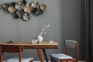 Modern ve şık yemek odaları, göz alıcı ahşap masa, zarif sandalyeler ve tasarım dekorasyonu. Şablon. Ev dekoru. Gri arka plan duvarı. İç tasarımın minimalist kavramı.