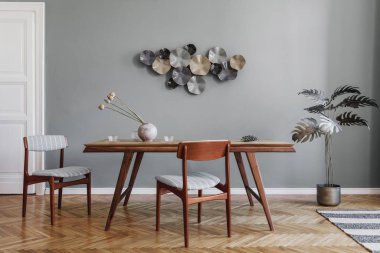 Modern ve şık yemek odaları, göz alıcı ahşap masa, zarif sandalyeler ve tasarım dekorasyonu. Şablon. Ev dekoru. Gri arka plan duvarı. İç tasarımın minimalist kavramı.