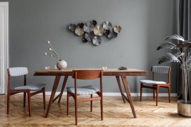 Modern ve şık yemek odaları, göz alıcı ahşap masa, zarif sandalyeler ve tasarım dekorasyonu. Şablon. Ev dekoru. Gri arka plan duvarı. İç tasarımın minimalist kavramı.