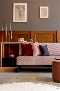 Tasarımlı pembe kanepe, zarif puf, kahve masası, bitkiler, yastıklar, dekorasyon, zarif kişisel aksesuarlar ve modern ev dekorunda poster çerçeveleri.. 