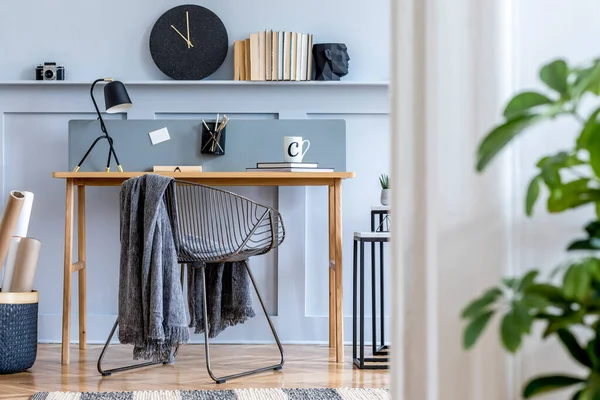 Scandinavian home office interior with wooden desk, design chair, wood panleing with shelf, plant, table lamp, office supplies and elegant accessories in modern home decor.