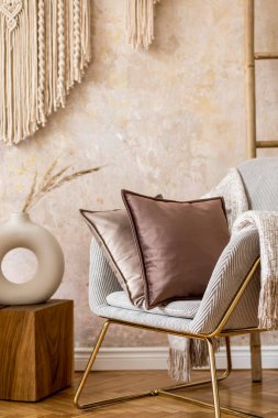 Interior design of oriental living room with modern armchair, macrame, velvet pillows, decorations and elegant personal accessories in stylish home decor.	