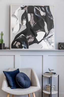 Tasarım gri koltuğu, yastıkları, mermer taburesi, tabloları, kaktüsü, dekorasyonu, siyah saati ve modern ev dekorunda özel aksesuarları olan şık bir oturma odası..