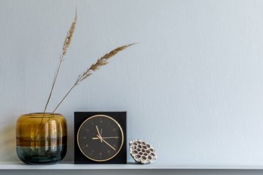 Ahşap rafta minimalist kompozisyon tasarım siyah saat vazoda kurumuş çiçekler ve şık oturma odasının iç kısmında zarif kişisel aksesuarlar. Boşluğu kopyala.