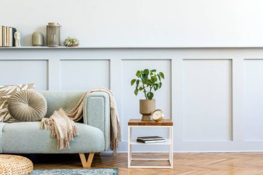 Tasarım kanepesi, kahve masası, bitki, kitaplar, dekorasyon, yastıklar, ekose, halı, ahşap paneller ve şık ev dekorasyonunda zarif persoanl aksesuarlar ile oturma odasının minimalist kompozisyonu.