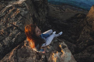 Yaz dağlarında uçurumun tepesinde deniz kenarında oturan kadın gezgin deniz ve doğa manzarasının tadını çıkarıyor. Cape Greco, Kıbrıs, Akdeniz. Gün doğumu