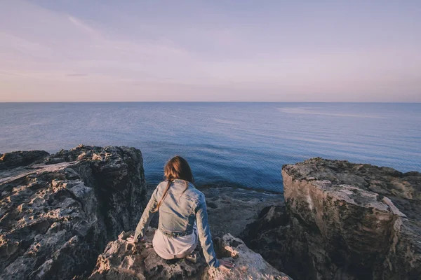 Női utazó ül közel a tenger tetején szikla a nyári hegyekben, és élvezi a kilátás nyílik a tengerre és a természetre. Cape Greco, Ciprus, Földközi-tenger. Napkelte — Stock Fotó