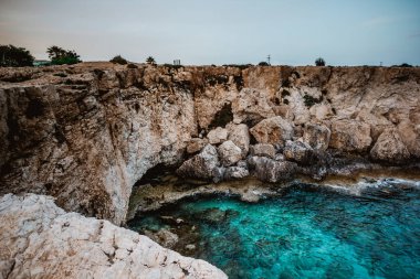 Kıbrıs, Cape Greco 'da mavi bir göl. Suyun birçok mavi tonu vardır. Kristal berrak su. Denizden çıkan keskin kayalar. Denizin sakin yüzeyi. Parlak ve güneşli bir gün.