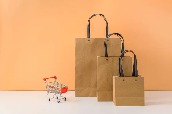 Bolsas de compras de papel y carrito de compras o carro sobre mesa blanca —  Fotos de Stock